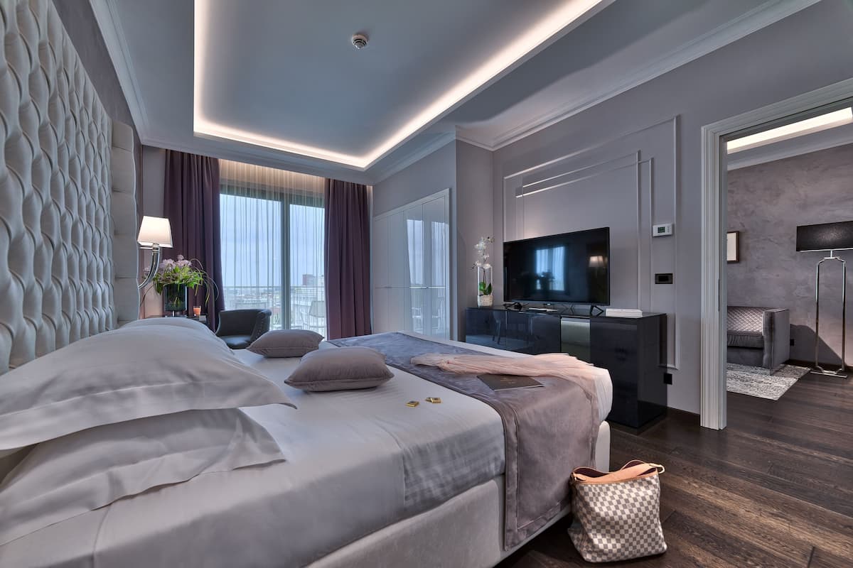 A modern hotel room with a large bed, a desk, a flat-screen TV, and a view of the city.