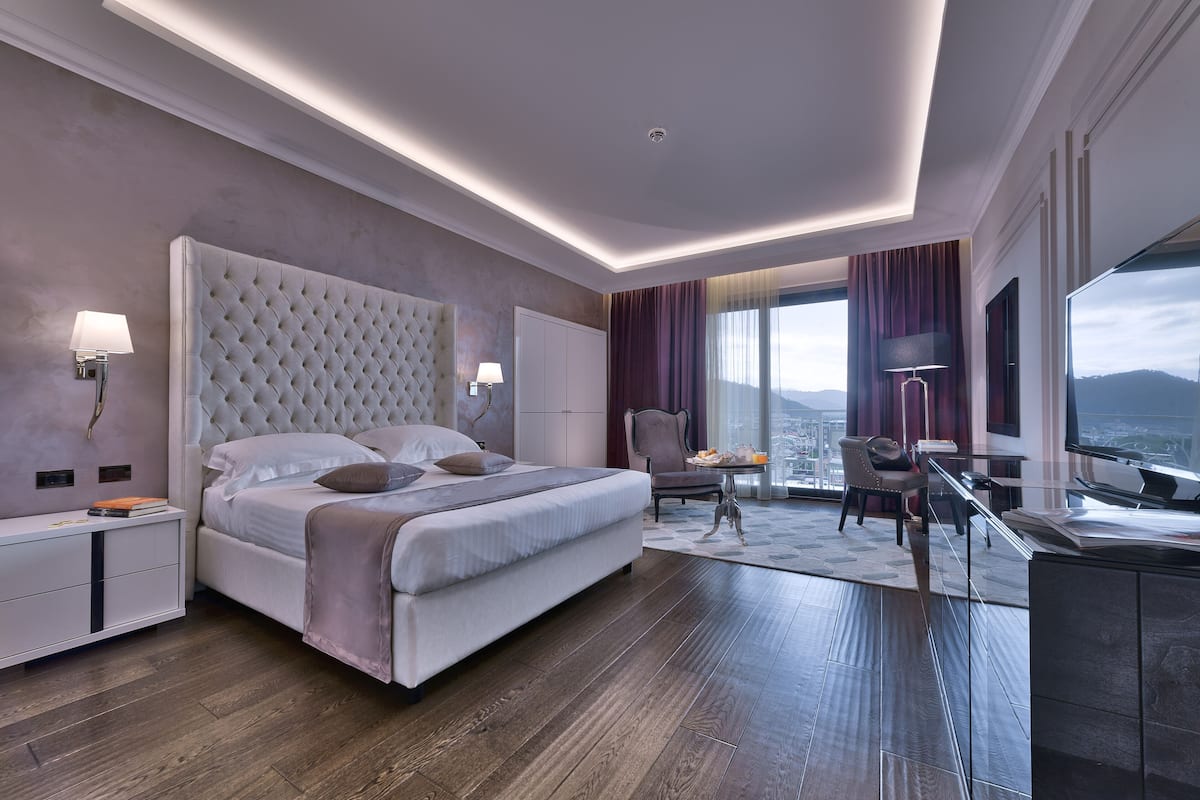 A modern hotel room with a large bed, a desk, and a view of the city.