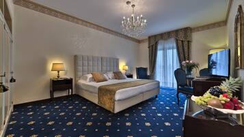 Quarto de hotel com uma cama grande, duas mesas de cabeceira com luminárias, um candelabro, uma escrivaninha com computador e uma fruteira em um aparador.