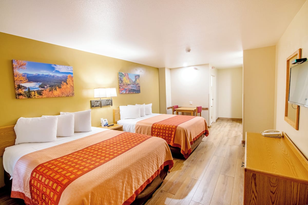 Ein Hotelzimmer mit zwei Betten, einem Schreibtisch, einem Stuhl und Bildern an den Wänden.