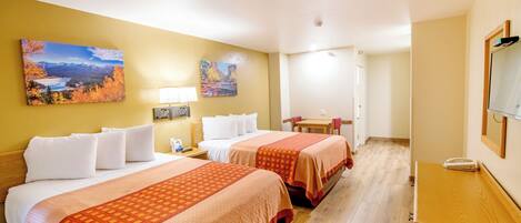 A hotel room with two beds, a desk, a chair, and artwork on the walls.