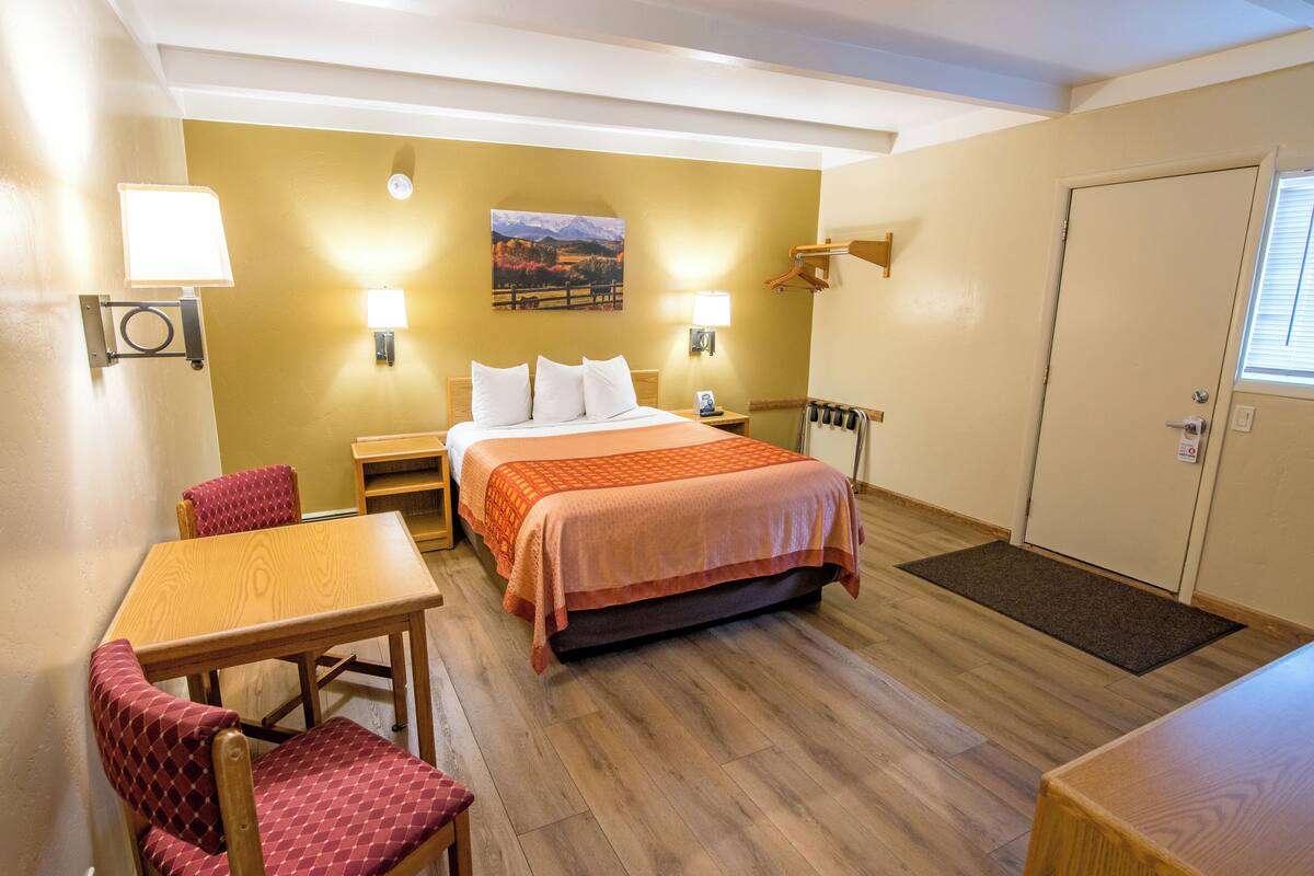 Ein Hotelzimmer mit einem Bett, zwei Nachttischlampen, einem Holztisch mit einem Stuhl, einer Tür und einem Fenster.
