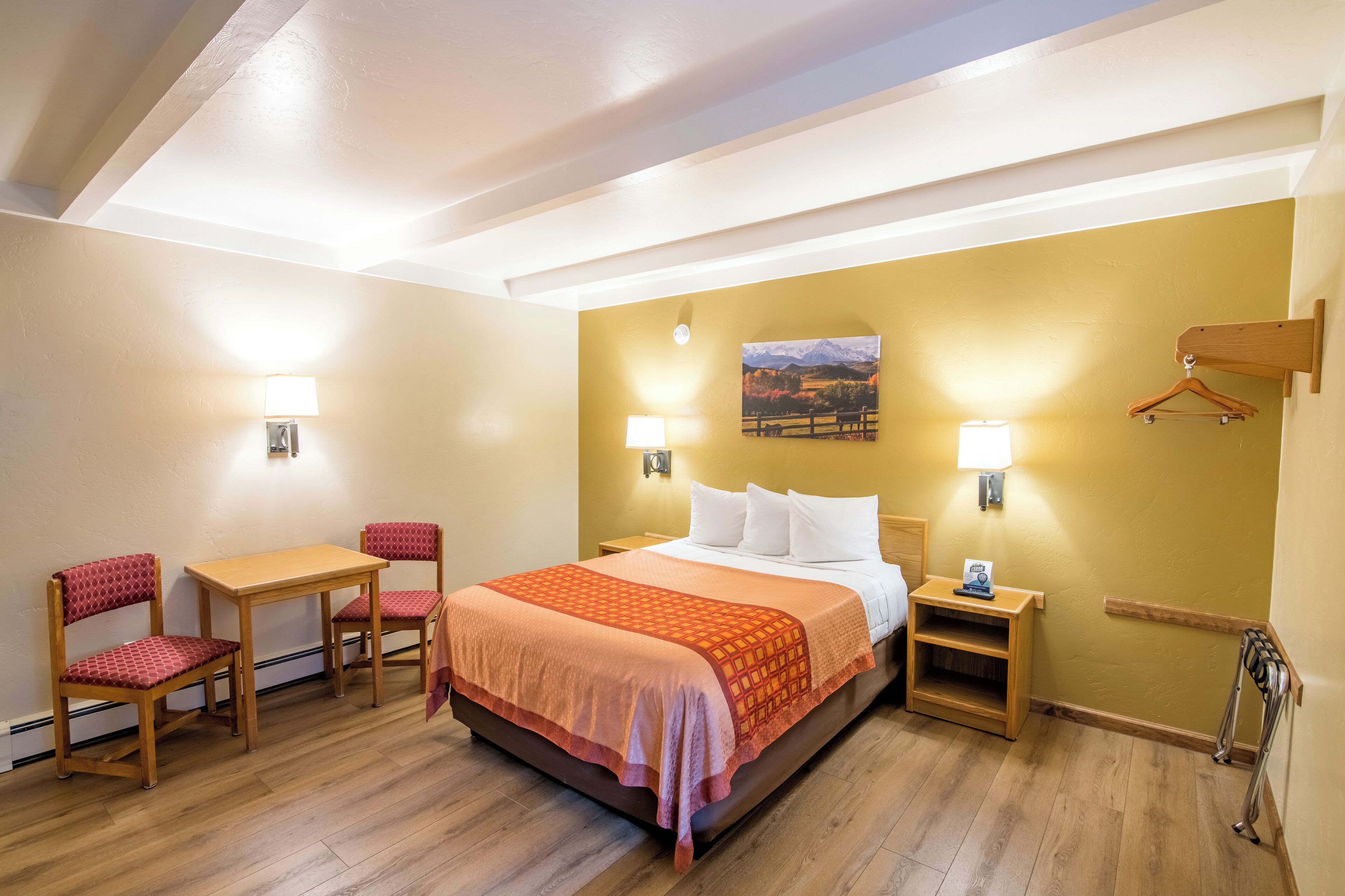 A hotel room with a bed, two chairs, a table, and a nightstand.