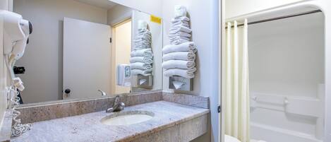 A bathroom with a granite sink, a mirror, a towel rack, a hand dryer, a toilet, and a shower.