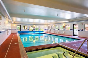 Ein Hallenbad mit blau und rot gefliestem Boden, klarem Wasser und einem blauen Rettungsschwimmerstuhl.