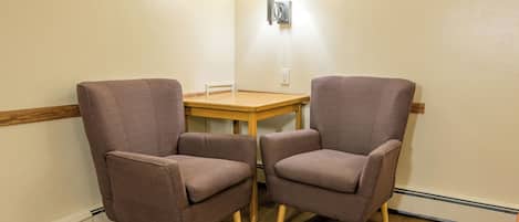 A room with two brown armchairs, a wooden table, and a wall-mounted lamp.