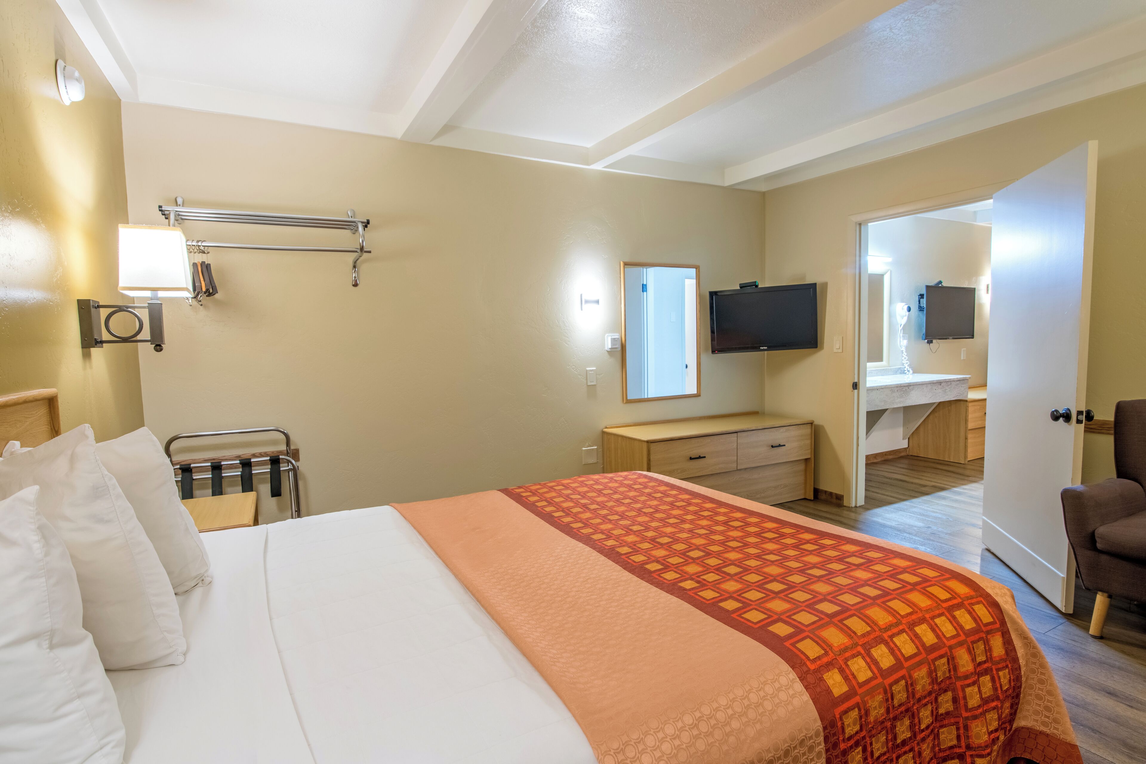 Ein Hotelzimmer mit Bett, Schreibtisch, Stuhl, Fernseher und einem durchgegangenen Tür sichtbaren Badezimmer.