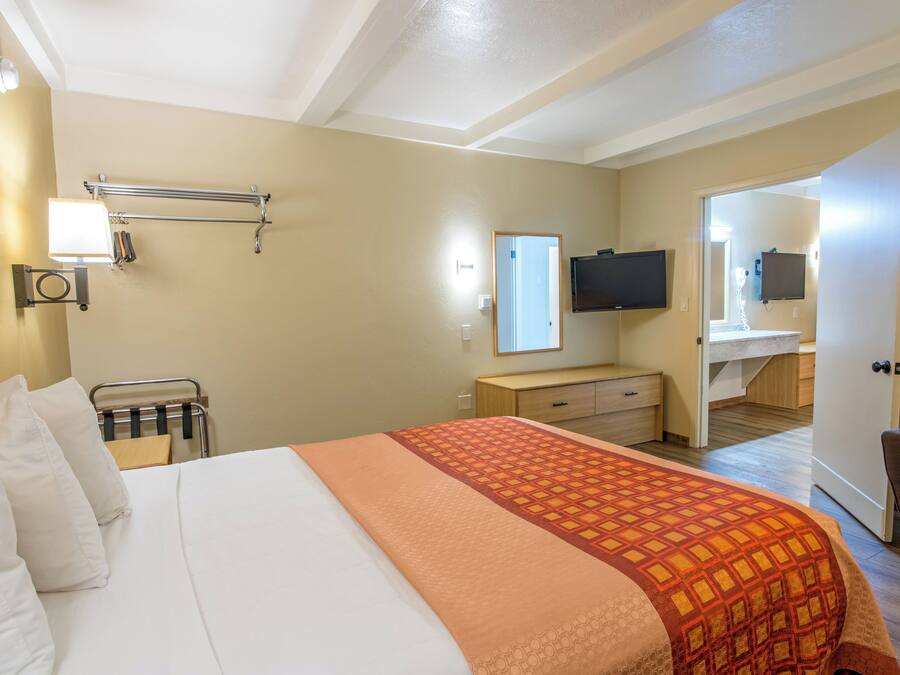A hotel room with a bed, a desk, a chair, a TV, and a bathroom visible through an open door.