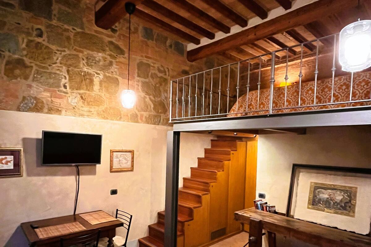 A cozy interior with a wooden staircase leading to a loft, a dining area with a table and chairs, and a flat-screen TV mounted on the wall.