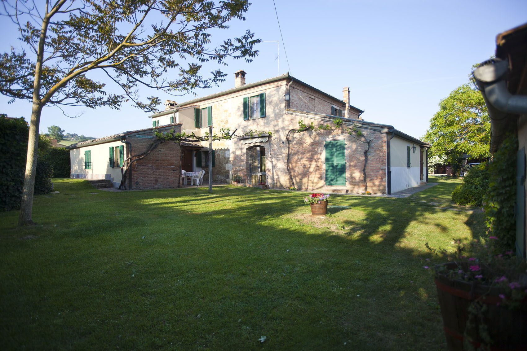 Ein zweigeschossiges Haus mit Backsteinfassade, grünen Fensterläden und einem kleinen Vorgarten mit Tisch und Stühlen.
