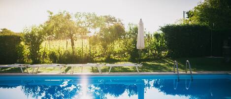 Una piscina al aire libre, sombrillas, sillones reclinables de piscina