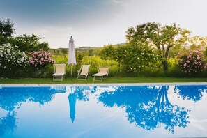 Une piscine aux eaux cristallines, agrémentée de trois chaises longues et d’un parasol blanc.