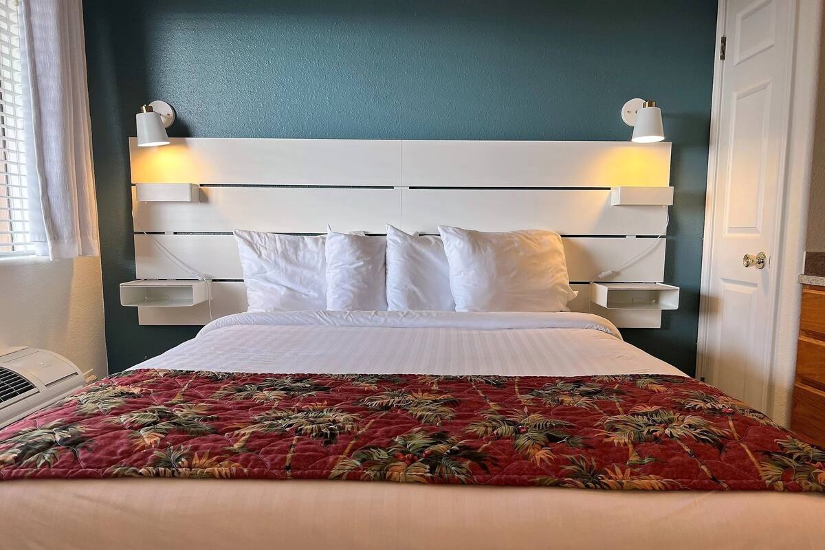A bed with a floral-patterned bedspread, a white headboard with wall-mounted lights, and a white bedside table.