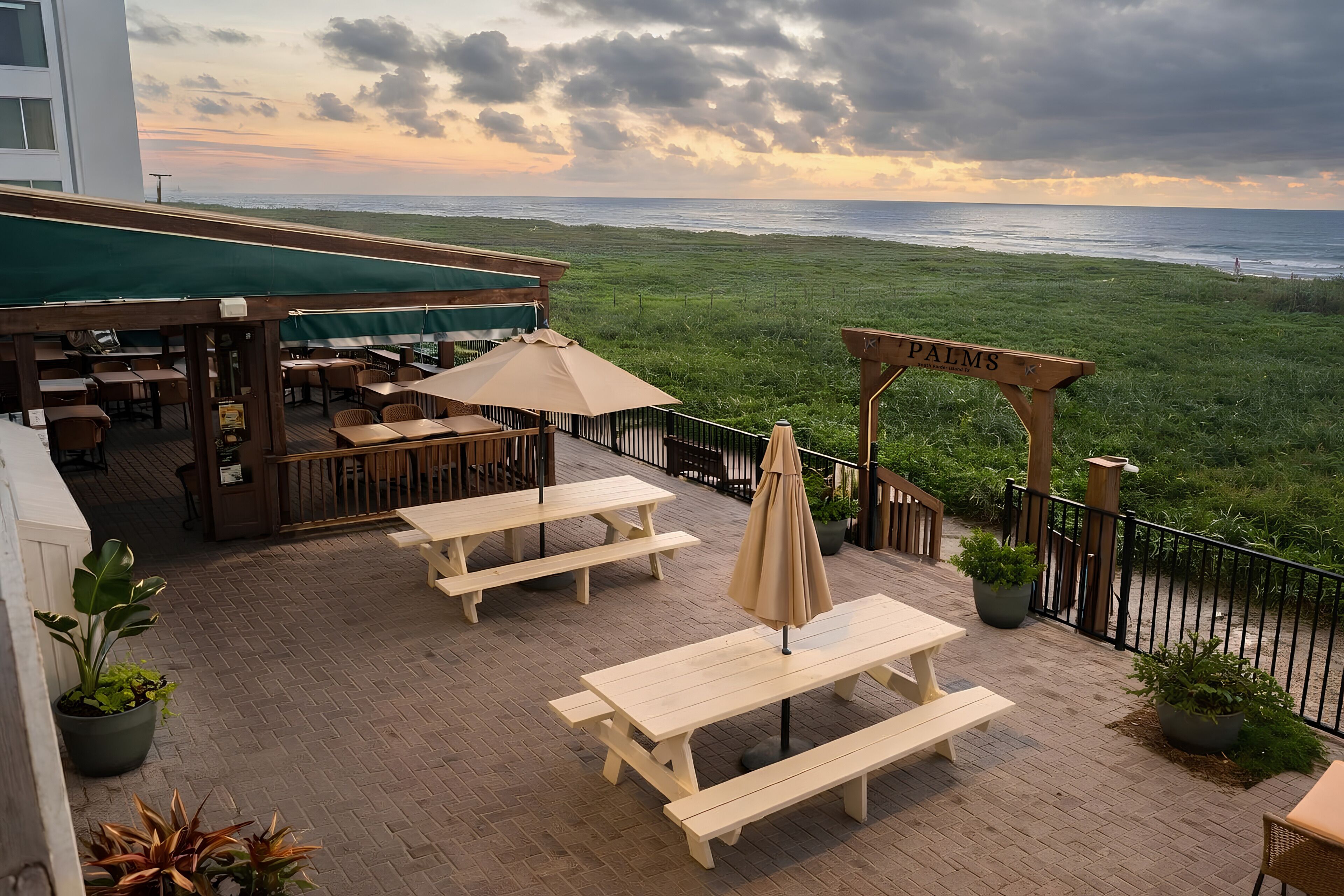 Une terrasse avec des tables et des bancs en bois, un auvent vert et une enseigne sur laquelle on peut lire « PILMS ».