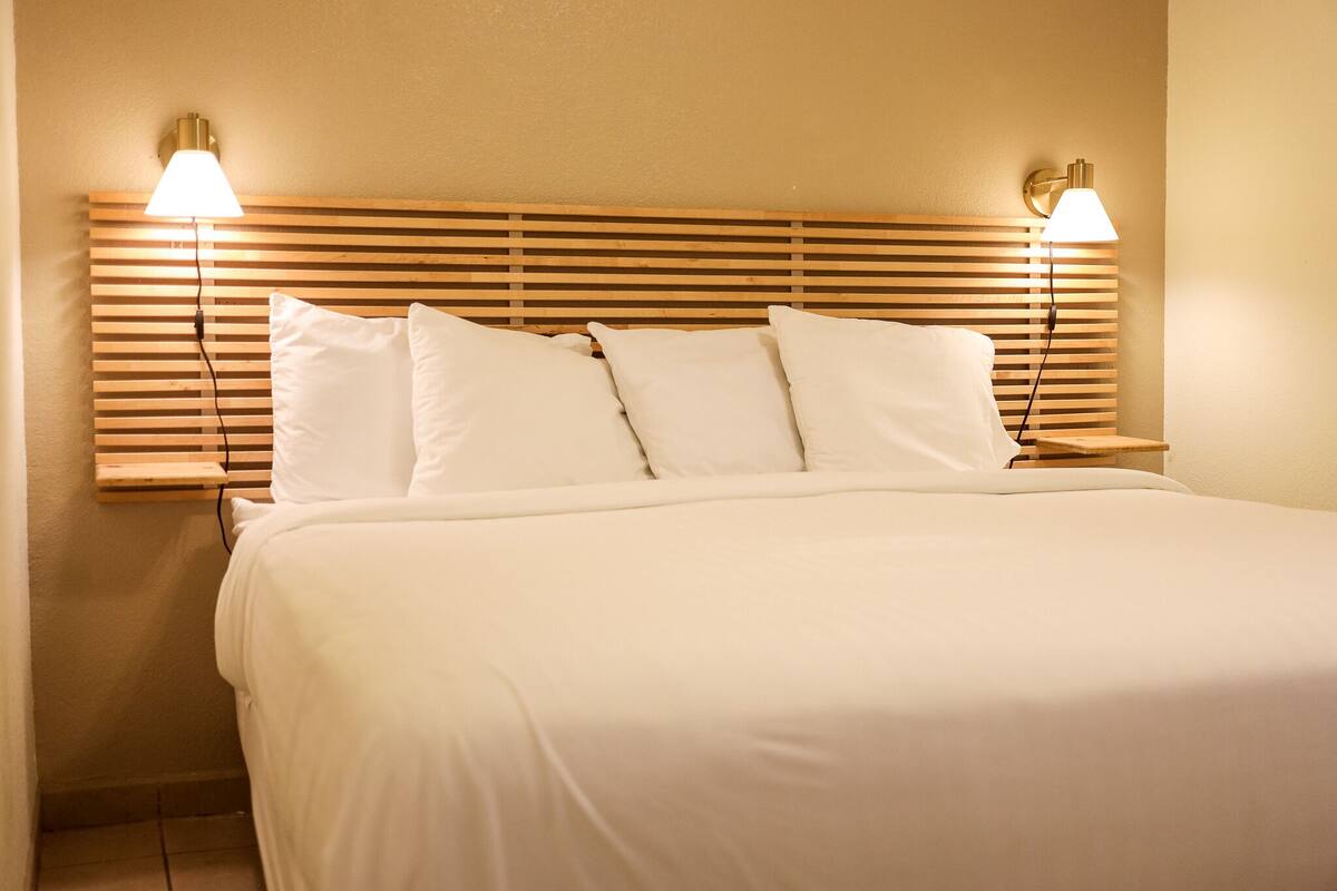 A neatly made bed with white linens and a wooden headboard with horizontal slats.