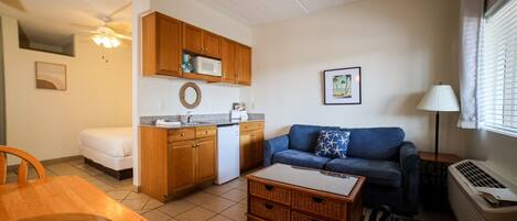 A compact living space with a kitchenette, a blue sofa, a dining table, and a ceiling fan.