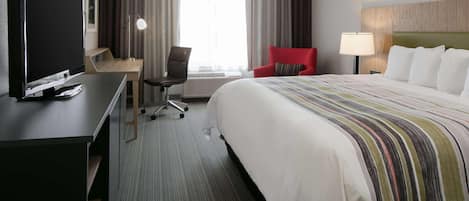 A hotel room with a bed, a desk with a TV, a chair, and a lamp.