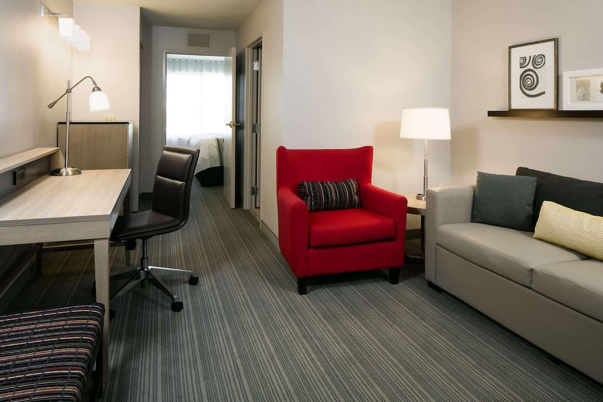 Ein Hotelzimmer mit Schreibtisch, einem roten Sessel, einer Couch und einer Lampe.