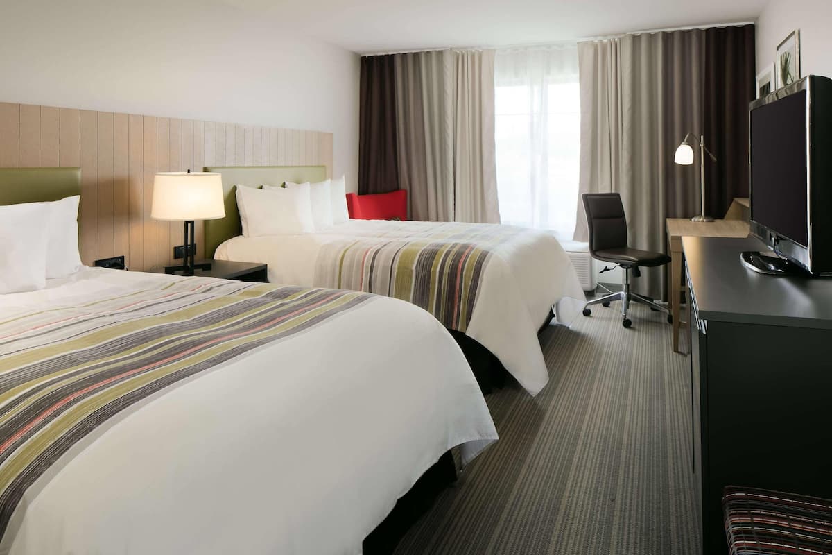 Ein Hotelzimmer mit zwei Betten, einem Schreibtisch mit Computer, einem Fernseher und einem Sessel.