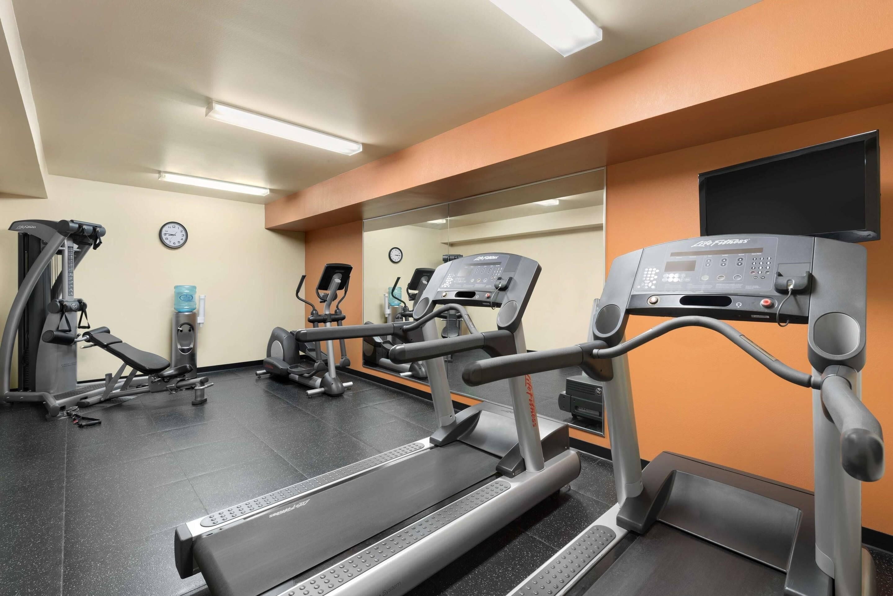 Un gimnasio con cintas de correr, elípticas y equipo de pesas.