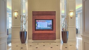 Un hall con un televisor de pantalla plana grande montado en un panel de madera, flanqueado por dos plantas grandes en macetas.
