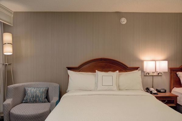 Una habitación de hotel con una cama grande, una silla, una mesita de noche y una lámpara.