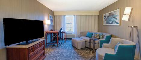 A hotel room with a flat-screen TV, a desk with a chair, a sofa, and a large window.