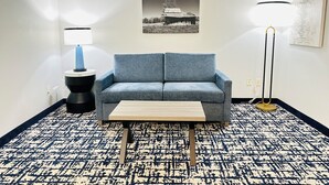 Una habitación con un sofá azul, una mesita de madera, una lámpara de pie negra y un cuadro colgado en la pared.