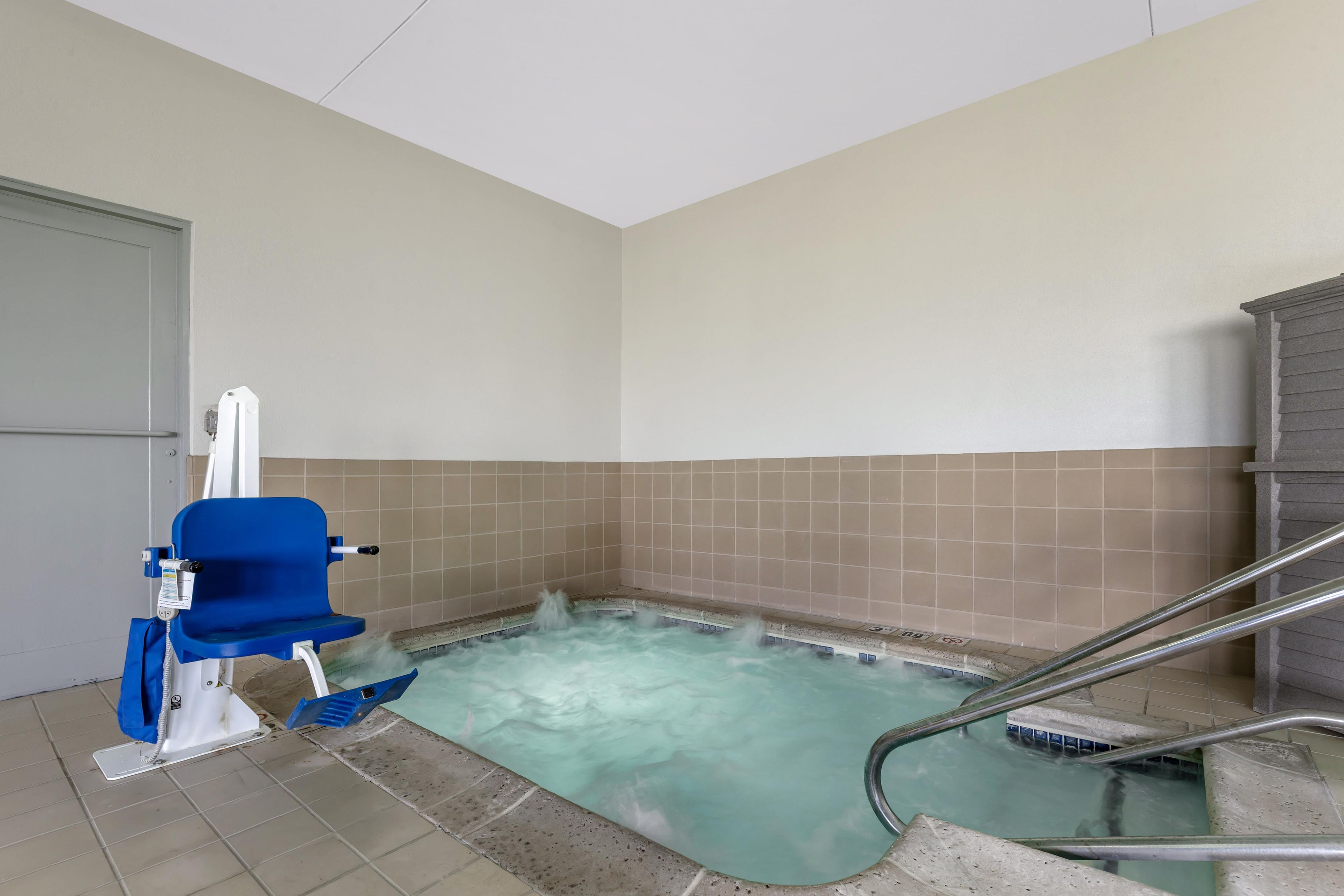 A small, rectangular hot tub with a blue chair and metal railings.