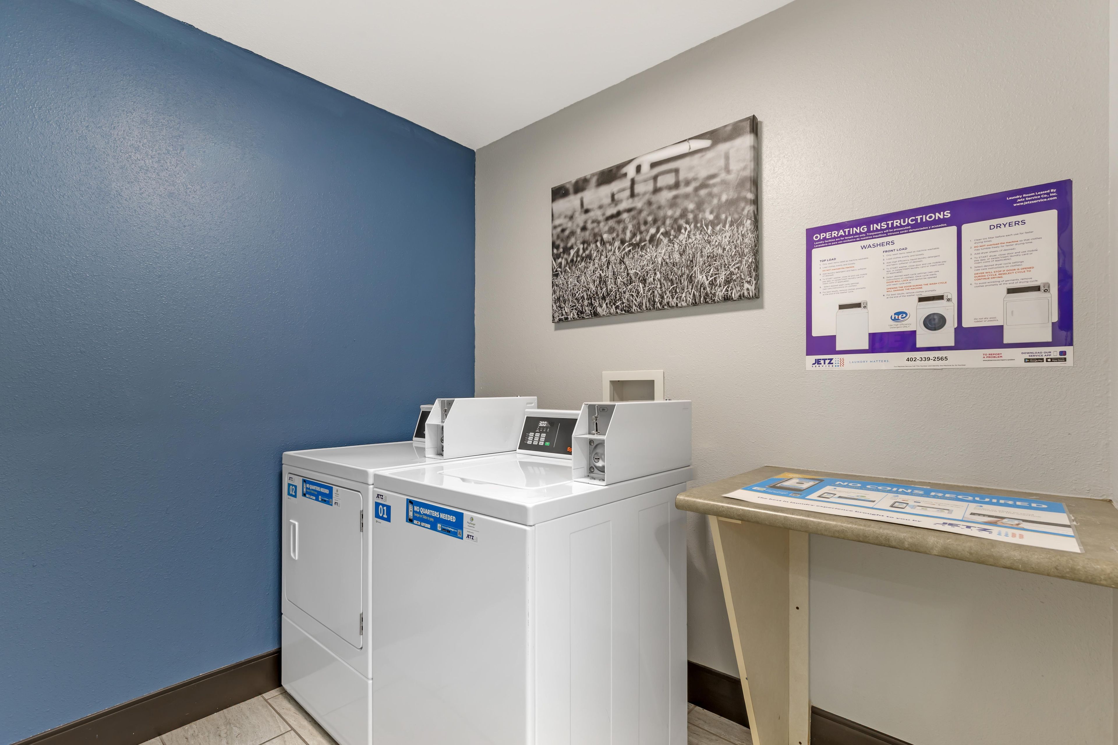A laundry room with a washing machine, a dryer, and informational posters on the wall.