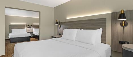 Quarto de hotel com uma cama grande, mesas de cabeceira, um espelho e uma luminária fixada na parede.