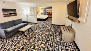 A hotel room with a sofa, a TV, a patterned carpet, a bed, and artwork on the walls. - Best Western Plus Omaha Airport Inn (Carter Lake)