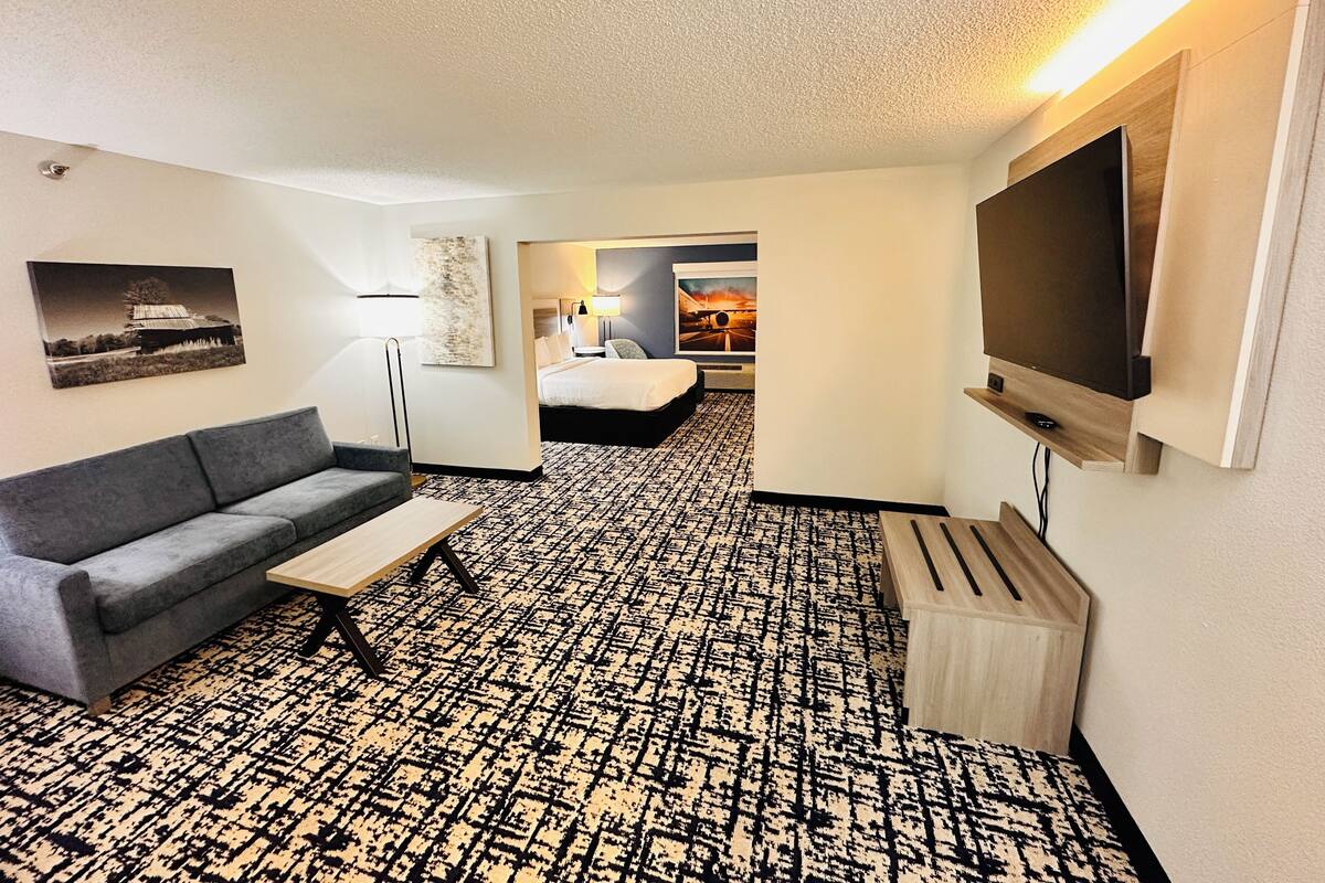 A hotel room with a sofa, a TV, a patterned carpet, a bed, and artwork on the walls.