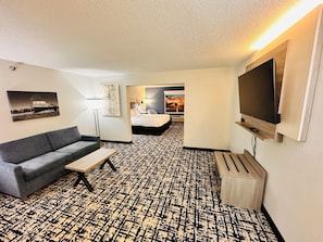 A hotel room with a sofa, a TV, a patterned carpet, a bed, and artwork on the walls. - Best Western Plus Omaha Airport Inn (Carter Lake)