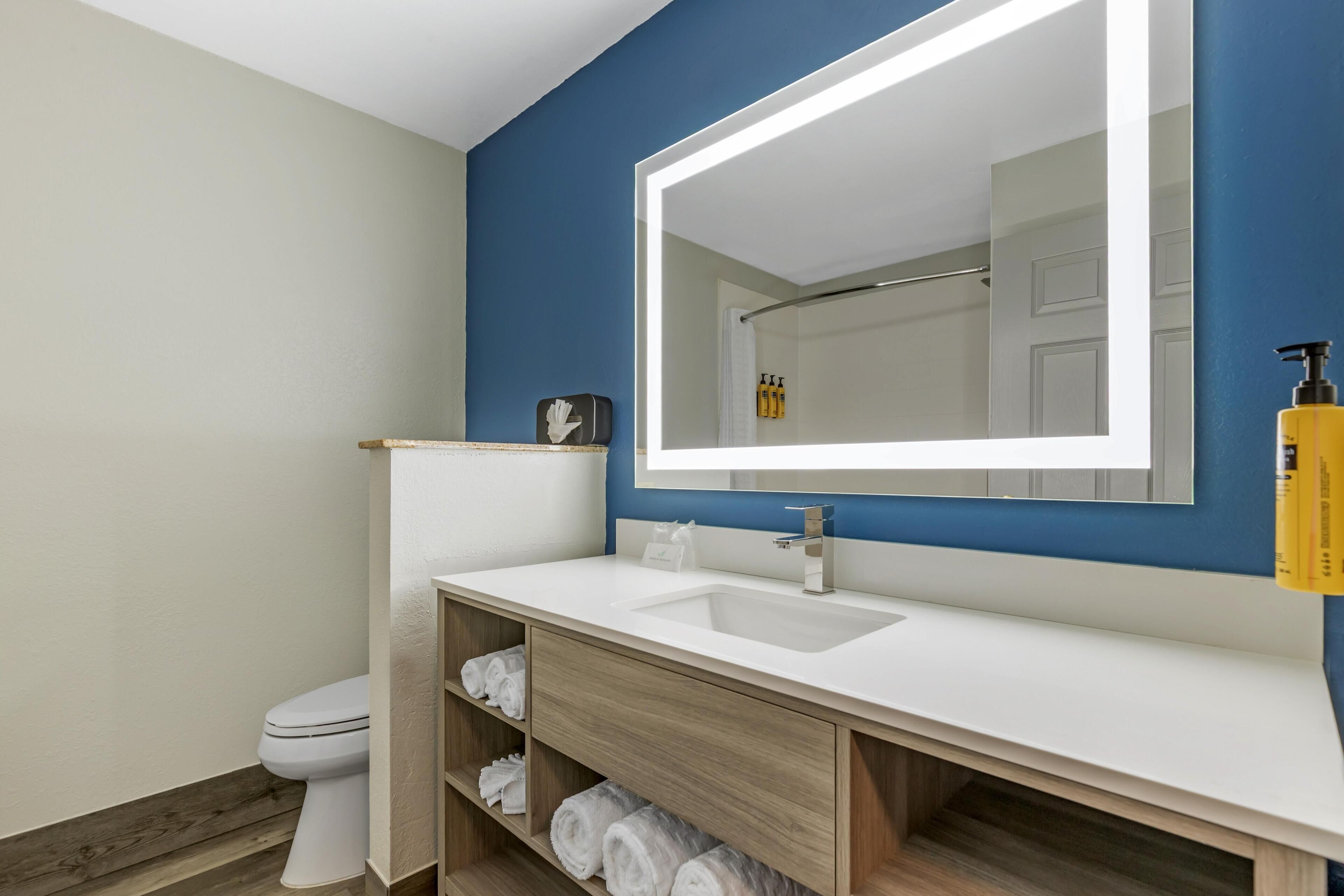 Een moderne badkamer met een wit wastafelmeubel, een grote spiegel en een houten dressoir.