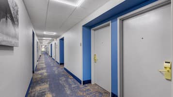 A hotel corridor with blue walls, white doors, and a patterned carpet.