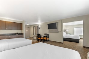 A hotel room with two beds, a dining table with chairs, a TV, and a bathroom visible through an open door. - Best Western Plus Omaha Airport Inn (Carter Lake)