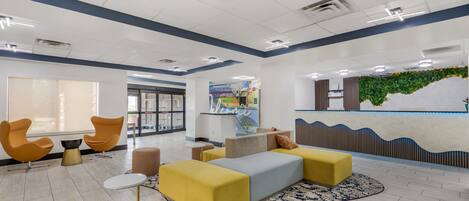 A modern lobby with seating areas, a reception desk, and a large window.