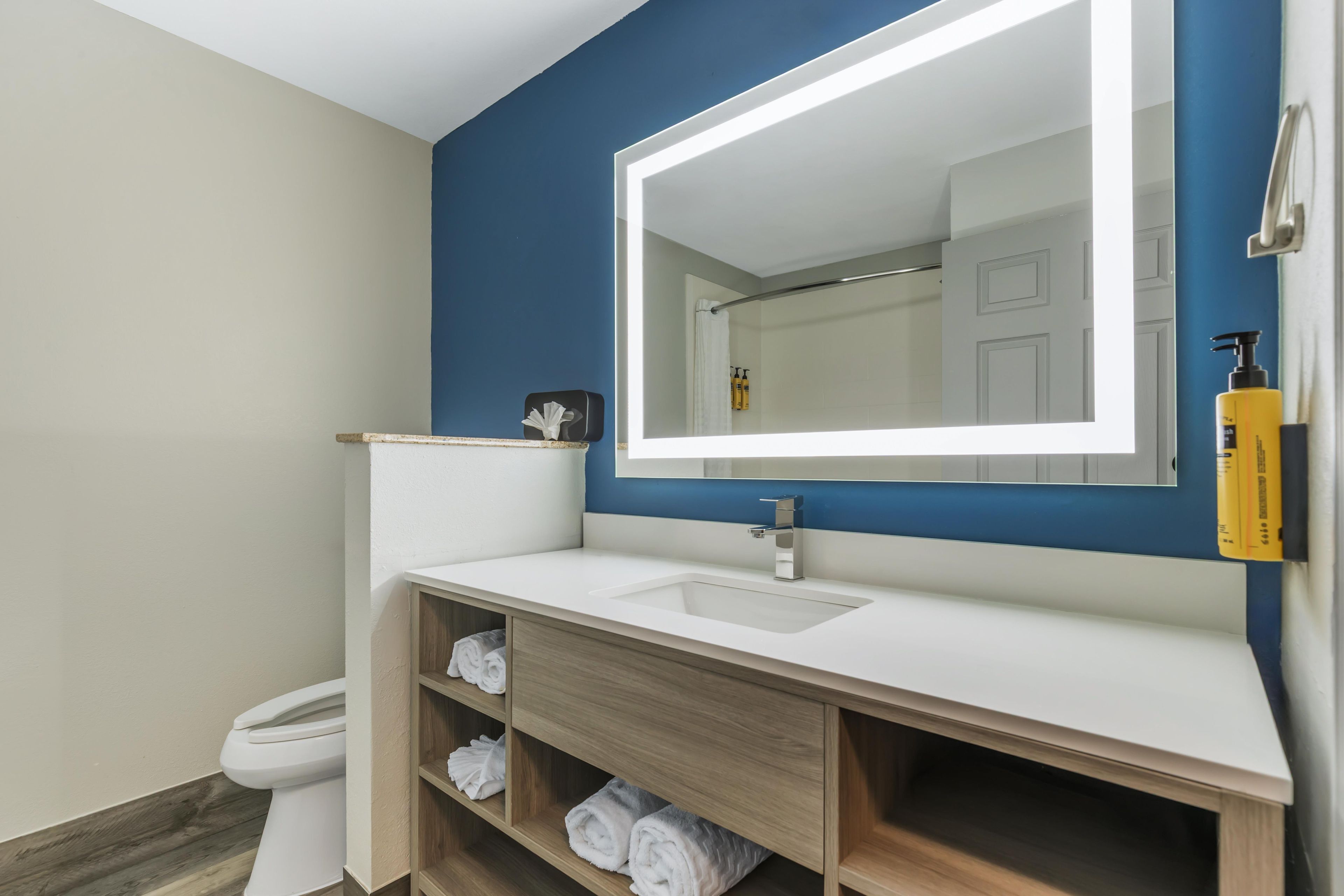Un baño moderno con un lavabo blanco, un espejo grande y un mueble de tocador de madera con estantes para toallas.