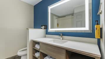 Un baño moderno con un lavabo blanco, un espejo grande y un mueble de tocador de madera con estantes para toallas.