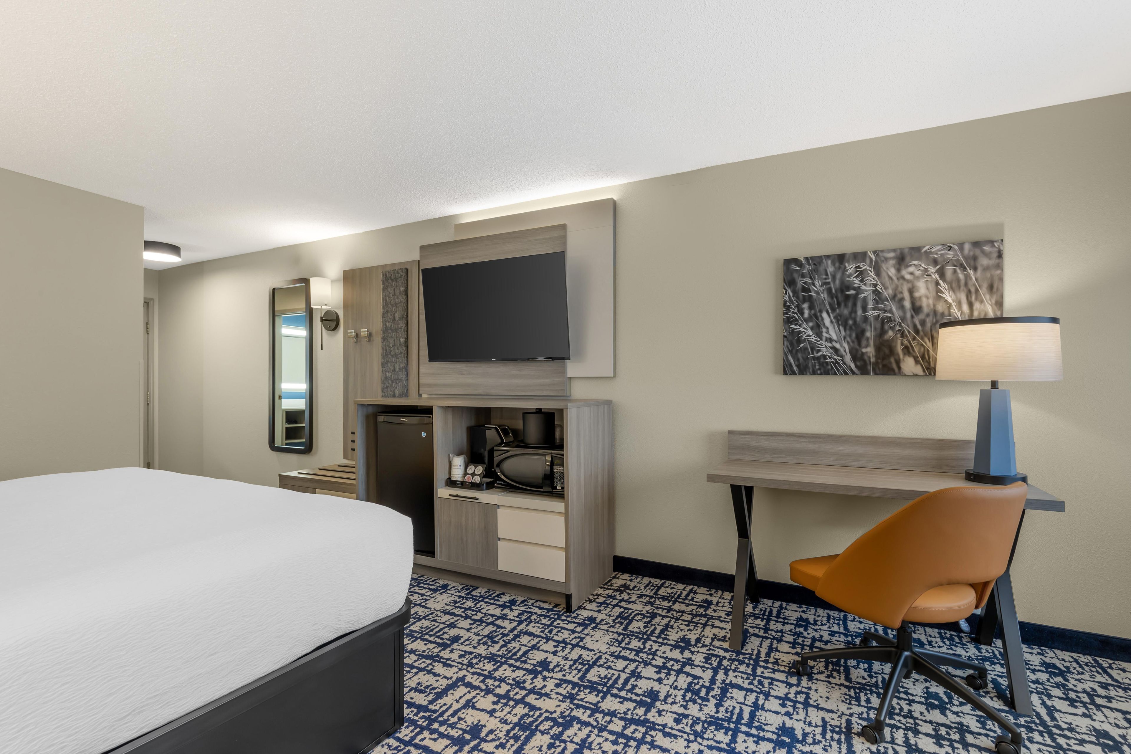 Quarto de hotel com cama, escrivaninha, cadeira, televisão e máquina de café.
