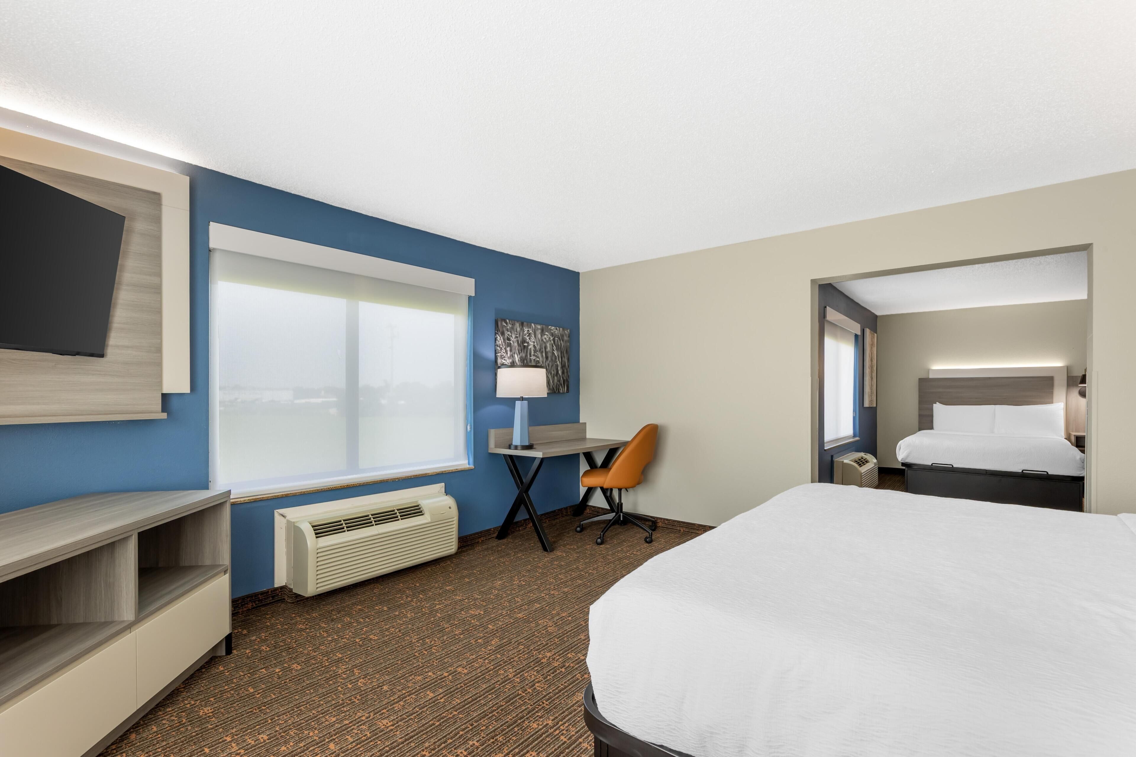 A hotel room with a bed, a desk, a chair, a TV, and a window.