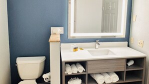 A bathroom with a toilet, a sink, a mirror, and a shelf with towels. - Best Western Plus Omaha Airport Inn (Carter Lake)