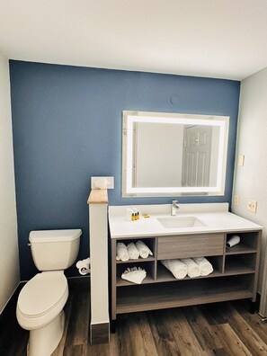 A bathroom with a toilet, a sink, a mirror, and a shelf with towels. - Best Western Plus Omaha Airport Inn (Carter Lake)