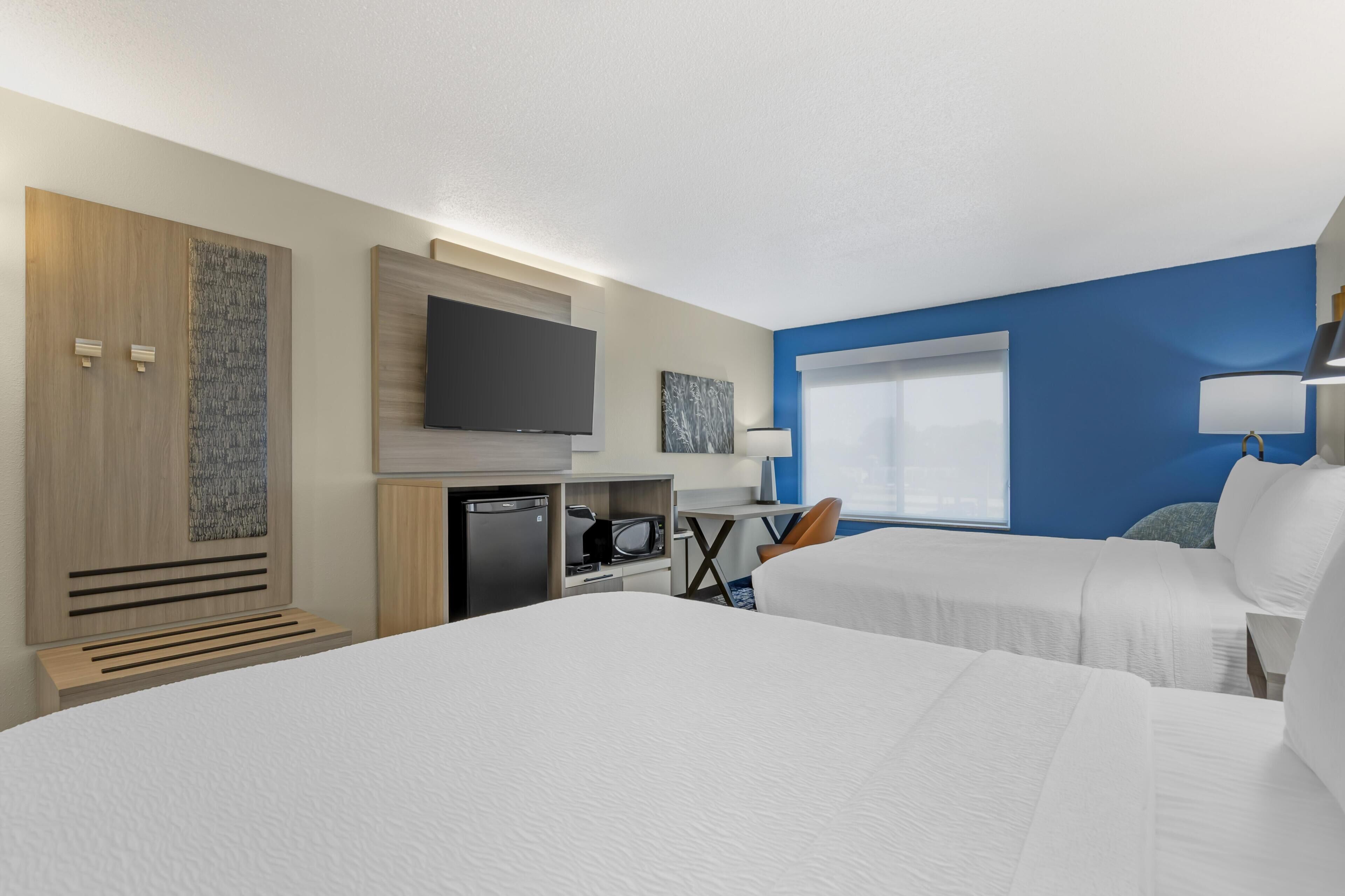 A hotel room with two beds, a flat-screen TV, a desk with a microwave, and a small refrigerator.