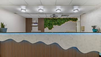 A reception desk with a marble top, a wooden slatted design below, and a green plant wall behind.