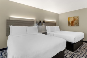 A hotel room with two beds, a nightstand, a wall-mounted lamp, and a painting. - Best Western Plus Omaha Airport Inn (Carter Lake)