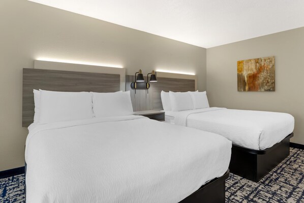 A hotel room with two beds, a nightstand, a wall-mounted lamp, and a painting. - Best Western Plus Omaha Airport Inn (Carter Lake)
