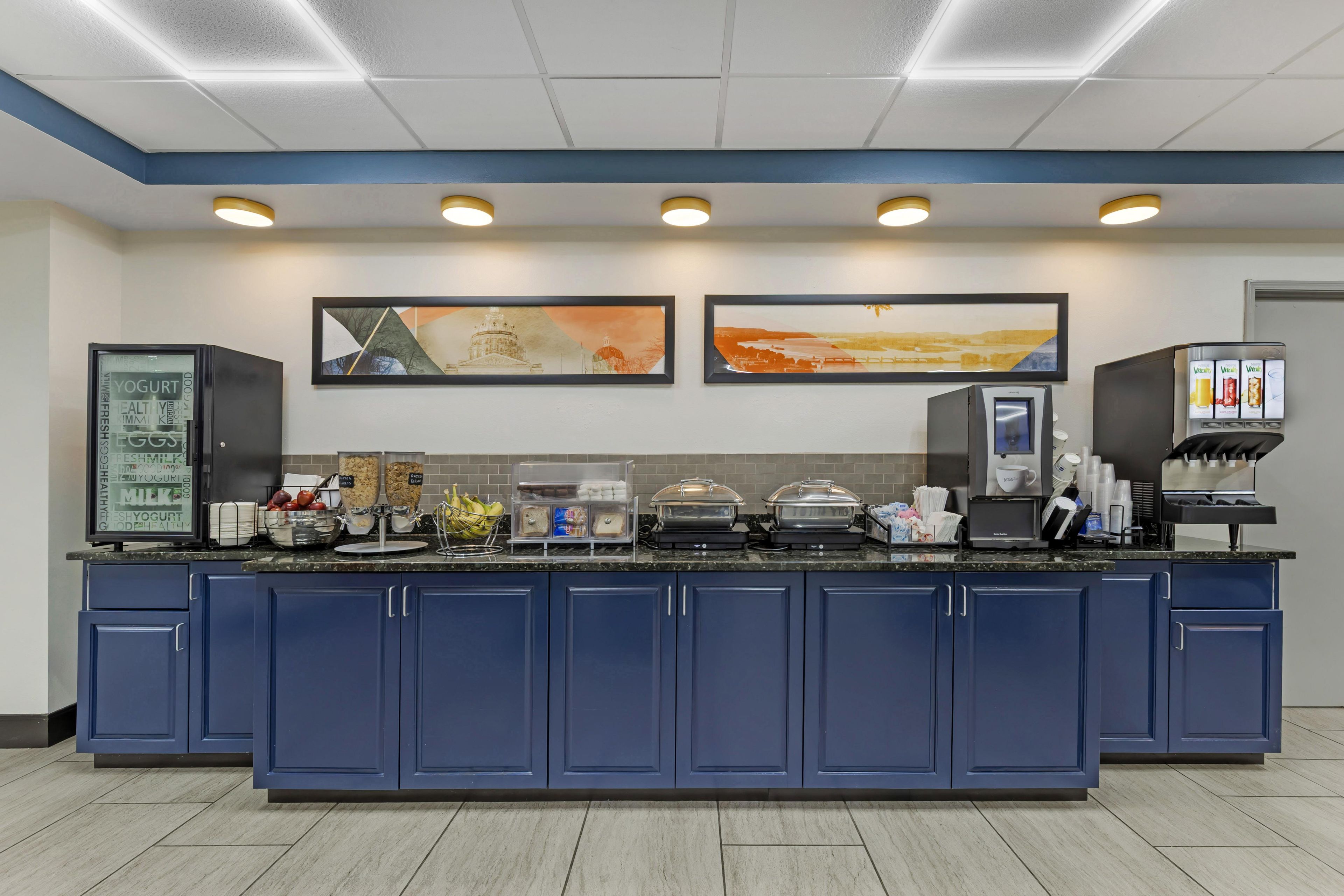 Ein Selbstbedienungsfrühstücksbuffet mit vielfältigen Speisen, einer Kaffeemaschine und zwei gerahmten Landschaftsbildern an der Wand.