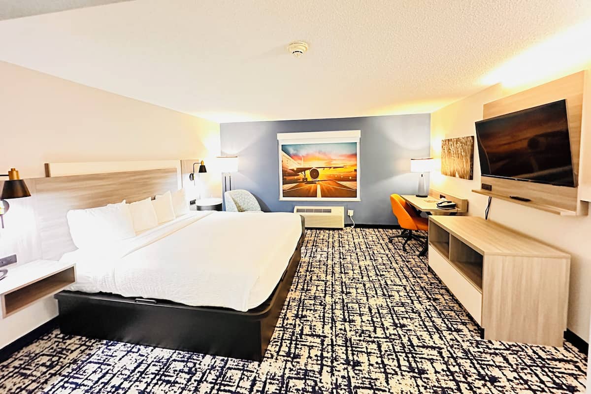 A hotel room with a bed, bedside tables, a desk, a chair, a TV, and a painting on the wall.
